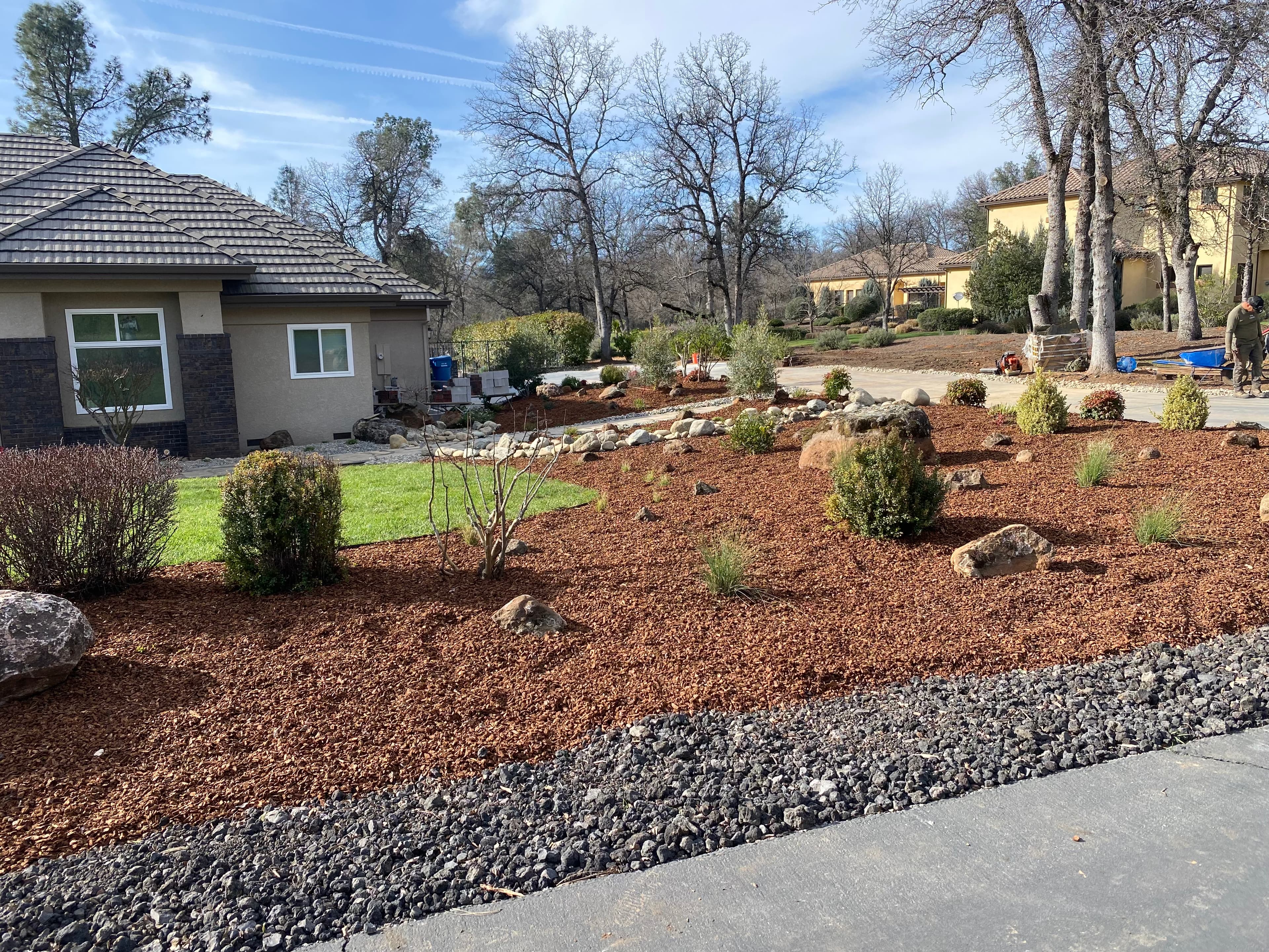Landscaped front yard with reddish-brown mulch, small shrubs, and rocks near a modern house.