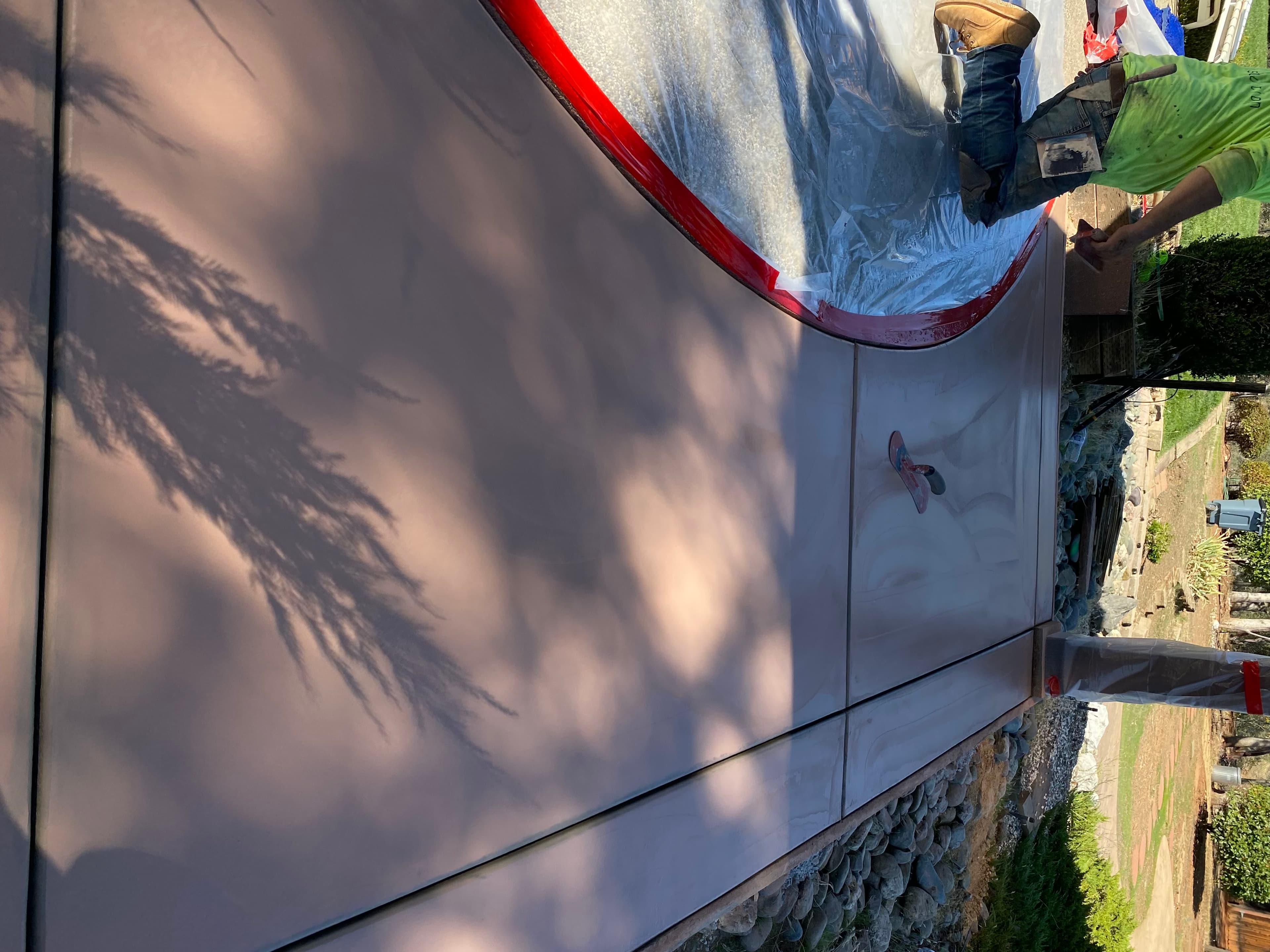 Worker finishing a smooth reddish-brown concrete patio with tree shadows and curved red borders.