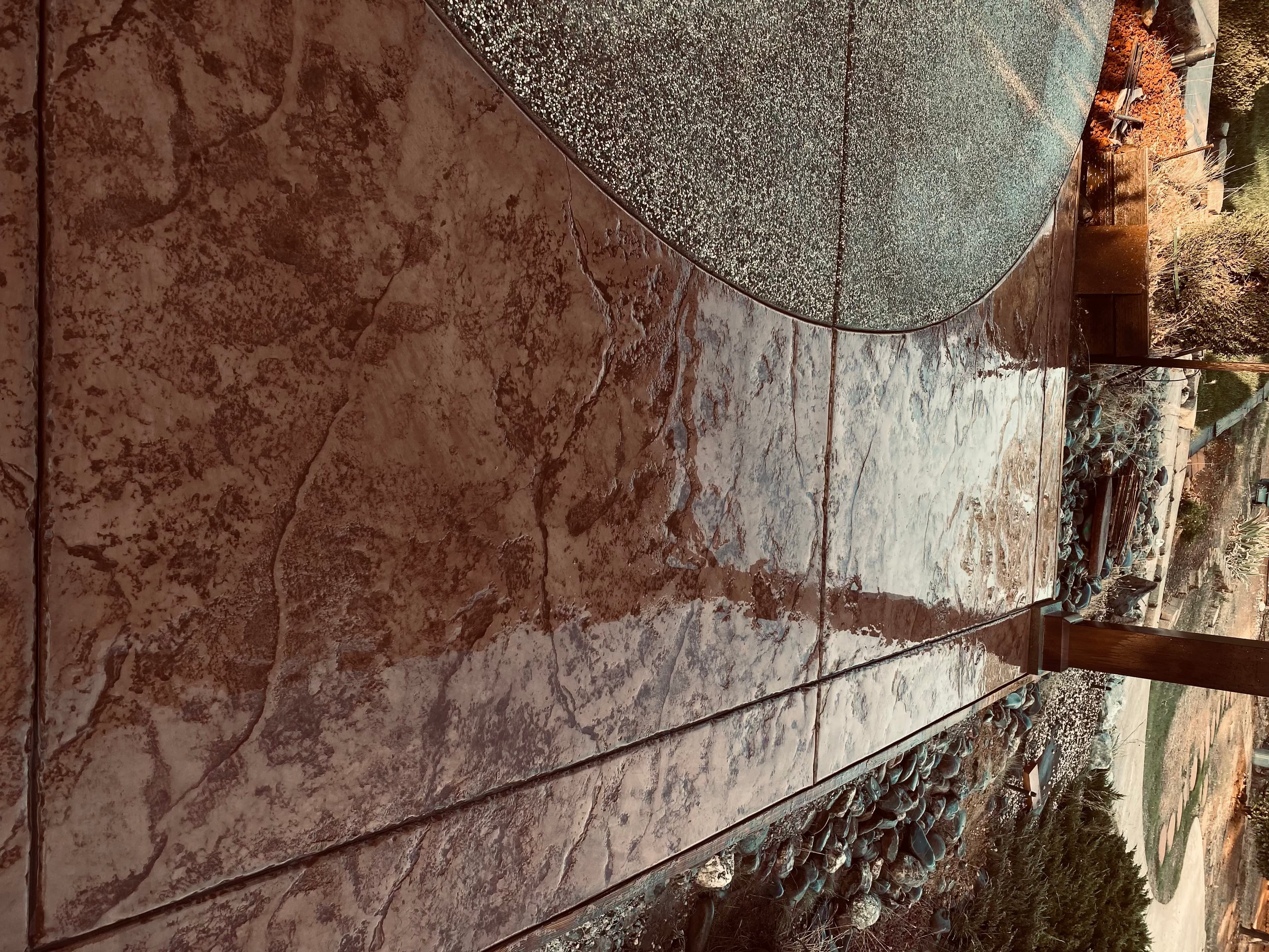 Glossy, reddish-brown stamped concrete with a stone-like texture bordering a grey aggregate patio surface.
