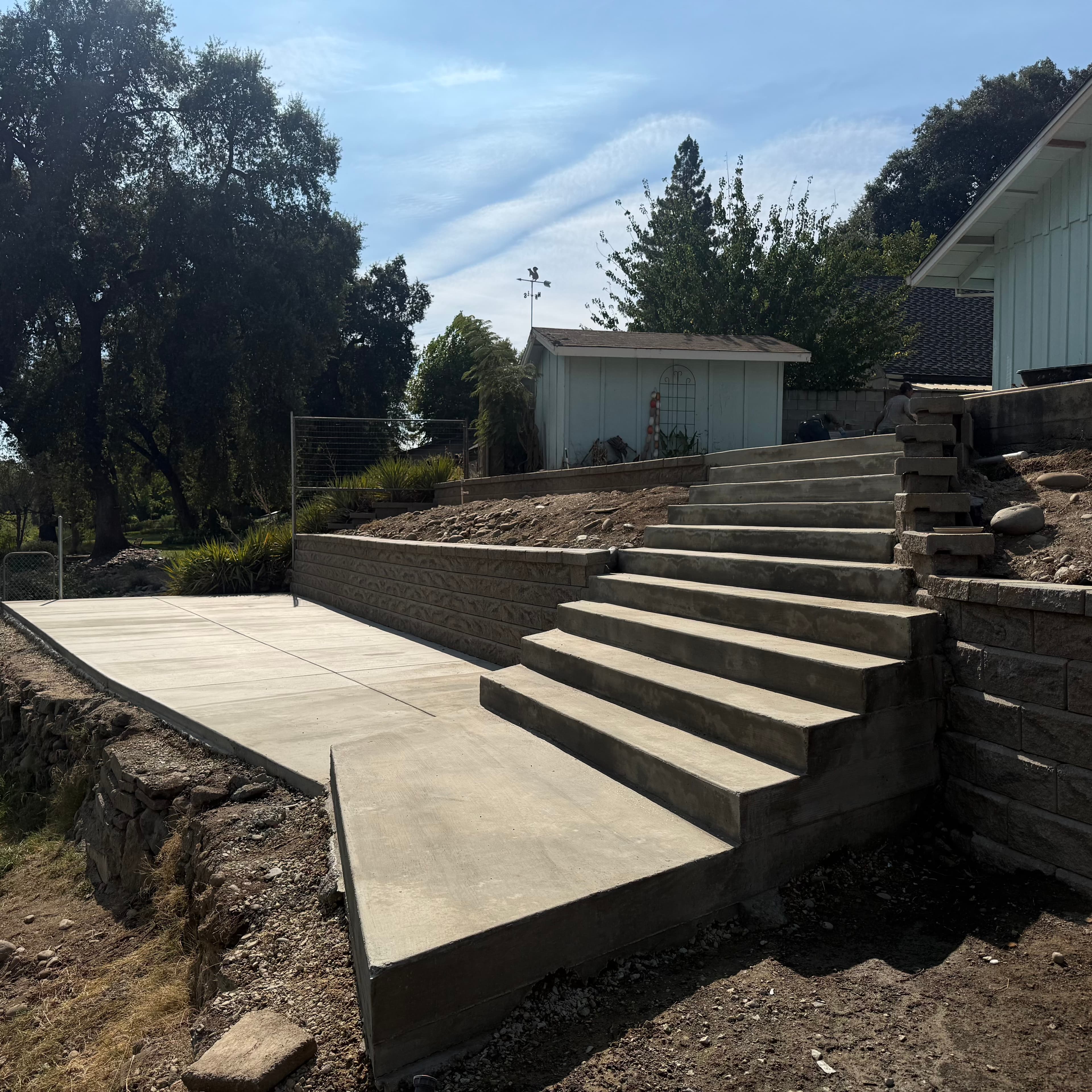 Wide concrete stairs and a patio landing built into a hillside with stone retaining walls.