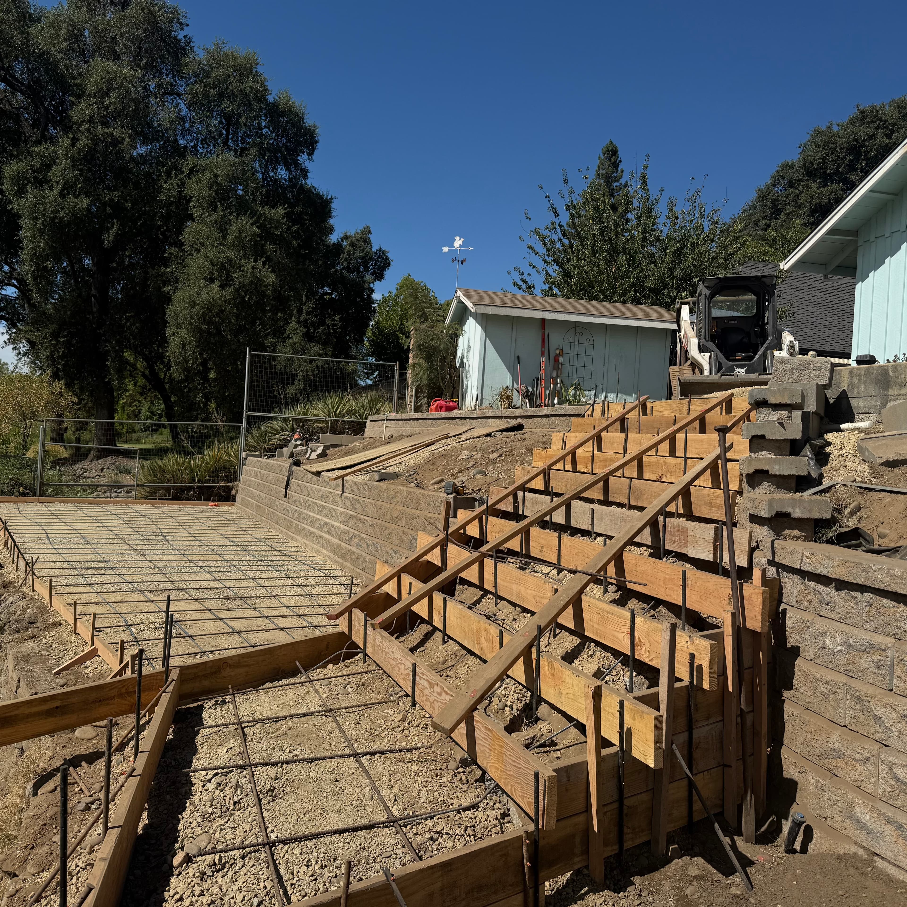 Wooden forms and rebar grids prepared for pouring concrete stairs and a patio outdoors.