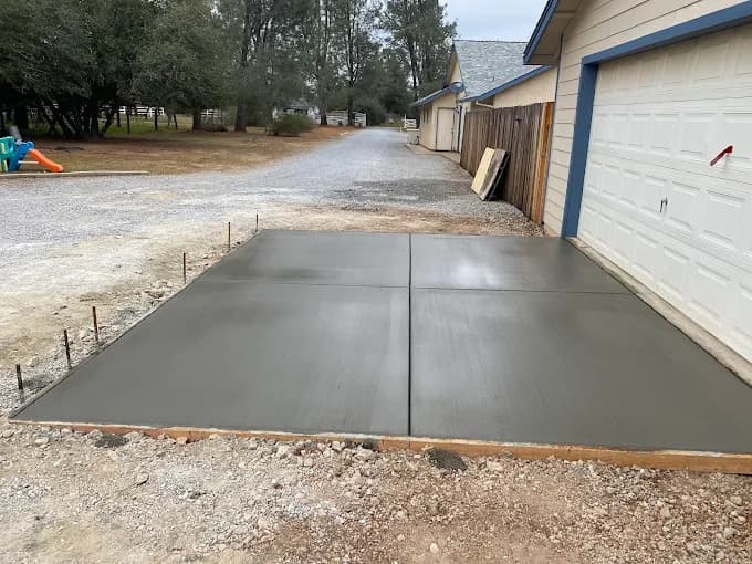 Newly poured and finished concrete slab with control joints in front of a white garage.