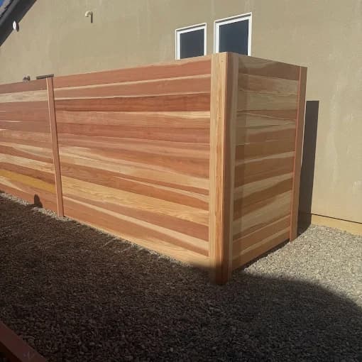 Horizontal cedar-toned wooden privacy fence with clean lines installed over a gravel-covered backyard area.