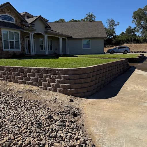 Brown stone block retaining wall bordering a tiered lawn in front of a house.